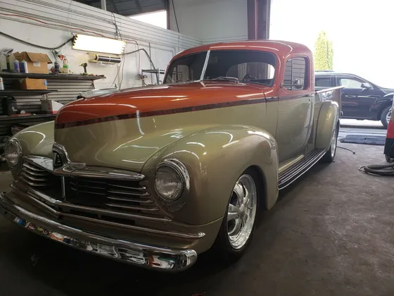 Orange and tan two-tone classic pickup with chrome wheels parked inside a shop bay