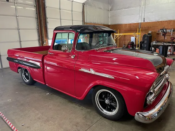 Red 1950s Chevrolet Apache pickup with a black roof and chrome bumper in the shop