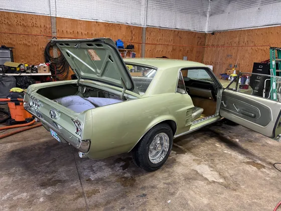 Light green 1960s Ford Mustang coupe with wire wheels, trunk and driver door open in the shop bay