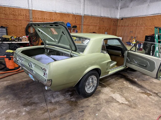 Light green 1960s Ford Mustang coupe with wire wheels, trunk and driver door open in the shop bay