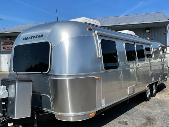 Airstream travel trailer with a bare aluminum body parked on the lot in front of the shop under a blue sky