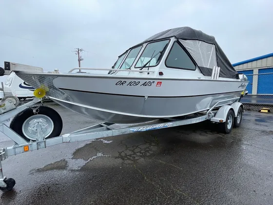 Silver aluminum boat with a black canopy on an EZ Loader trailer on wet pavement, port bow