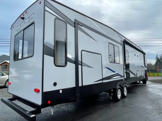 Gray Arctic Wolf fifth wheel with black skirt seen from the rear corner on wet pavement