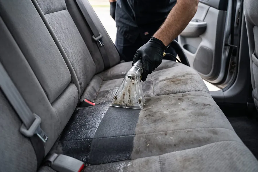 Extractor wand shampooing a gray cloth back seat, leaving a clean stripe through the dirt