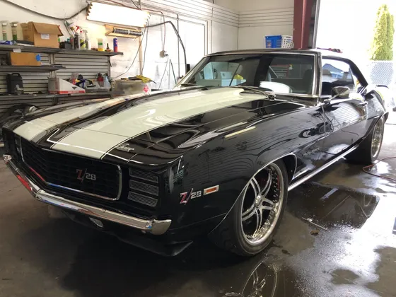 Black late 1960s Camaro Z/28 with white stripes and chrome wheels on a wet shop floor