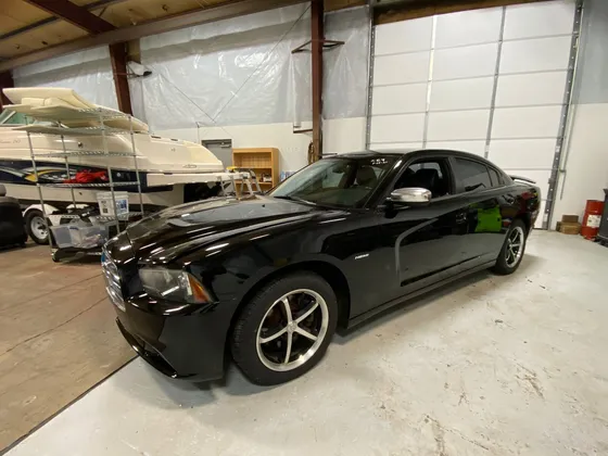 Front driver side of a black Dodge Charger with a Hemi badge in a shop bay