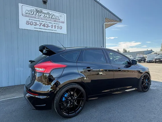 Black Ford Focus RS hatchback with blue brake calipers parked next to the shop wall