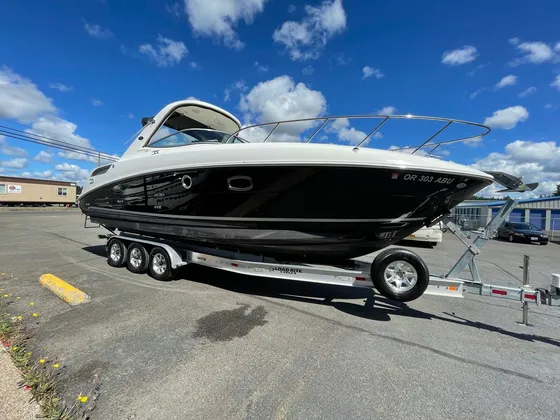 Cabin cruiser with a black hull and white deck on a triple axle trailer parked outside under a blue sky