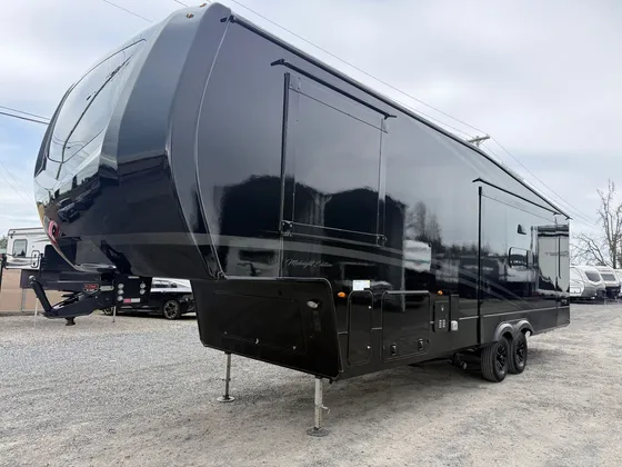 Black Midnight Edition fifth wheel trailer parked on a gravel lot, seen from the front driver side