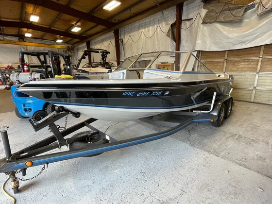 Black and silver open boat with a blue stripe on a gray trailer inside the shop