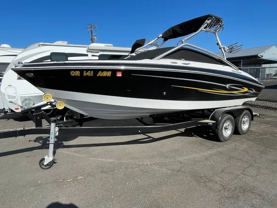 Black and white wake boat with a tower and yellow stripe sitting on its trailer