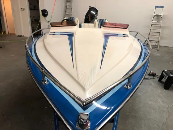 Front of a blue and cream open-bow boat with a chrome bow rail, sitting on a trailer in the shop