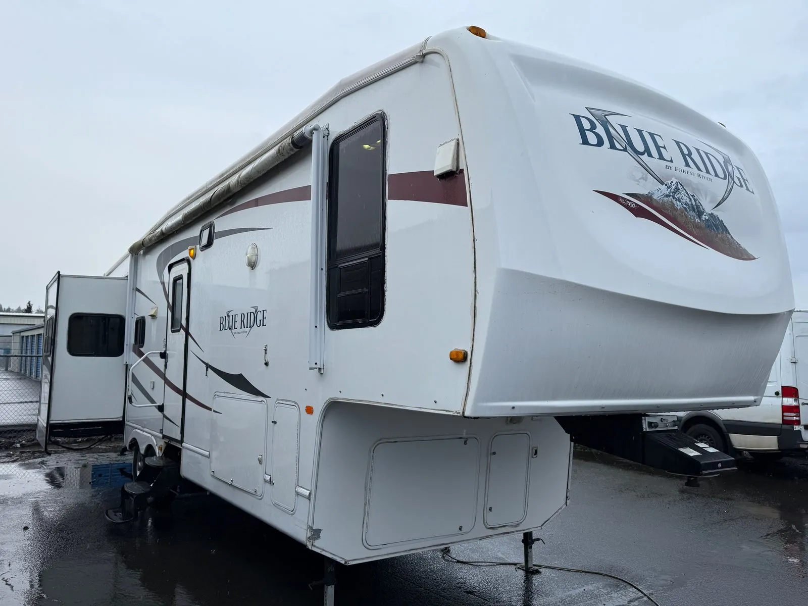 The same Blue Ridge fifth wheel with a clean front cap and side walls, parked on wet pavement