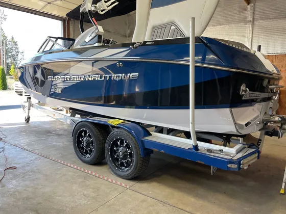 Blue and white Super Air Nautique wake boat on a tandem trailer inside the shop, seen from the rear quarter