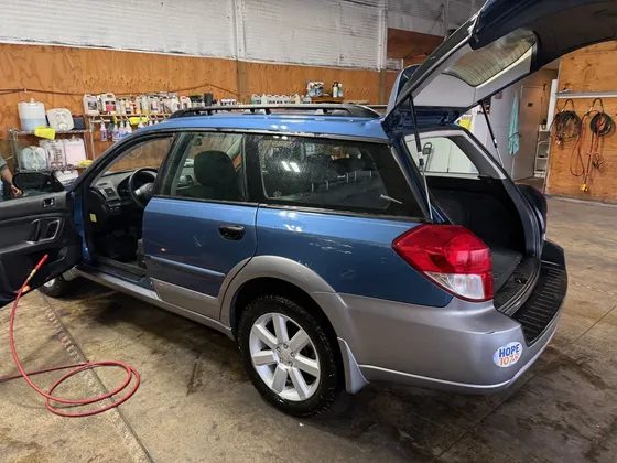 Blue station wagon with the driver door and tailgate open in the shop bay and an air hose on the floor