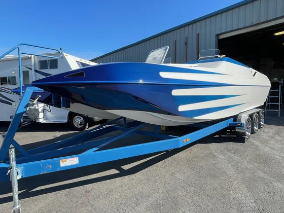 Blue and white open performance boat with a pointed bow on a blue trailer outside the shop