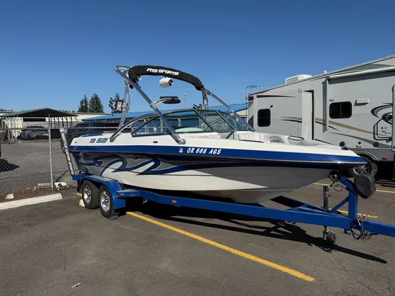 Blue and white wake boat with a tower on a blue trailer parked in the lot