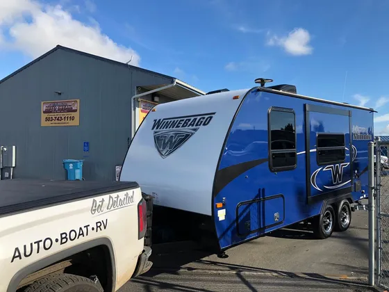 Blue and white Winnebago Micro Minnie travel trailer hitched behind the shop truck outside the shop