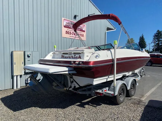Burgundy and white Solara boat with a burgundy bimini top on its trailer next to the shop wall