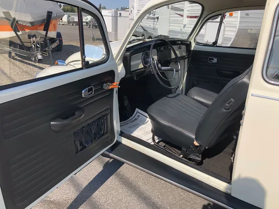 Black vinyl seats and dash of an older white VW Beetle seen through the open driver door