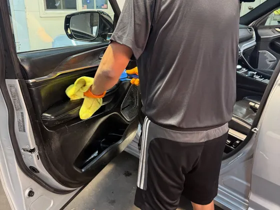 Worker in orange gloves wiping the inside door panel of a silver SUV with a yellow towel
