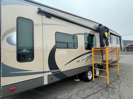 Man on yellow scaffolding wiping the upper side of a tan Eagle Premier fifth wheel outside
