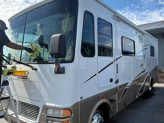 Worker wiping the windshield of a white and tan class A motorhome with a step ladder beside it