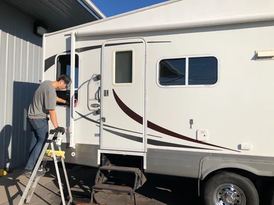 Worker on a step ladder wiping a window on the side of a white fifth wheel RV