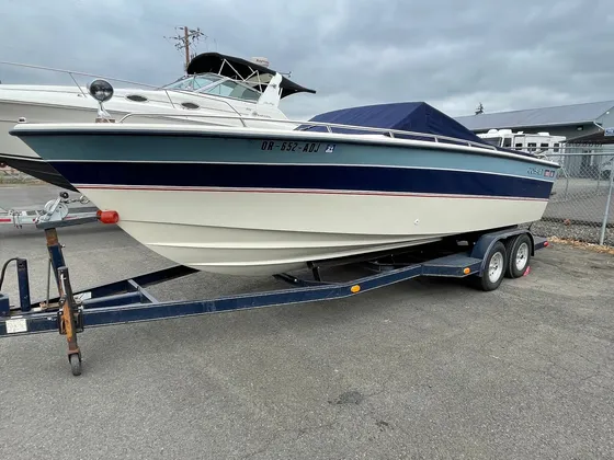 Navy, teal and cream Cobalt boat with a blue cover on a navy trailer parked outside under gray sky