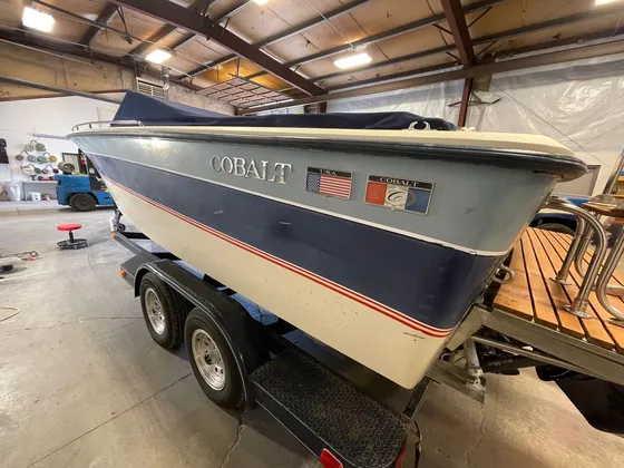 Faded navy and cream Cobalt boat hull on a trailer in the shop with a teak swim platform at the stern