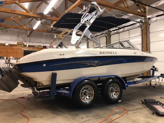 Cream and blue Reinell boat with a wake tower sitting on its trailer inside the shop