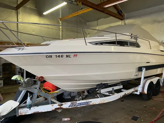 Cream cabin cruiser on a rusty trailer in the shop with a towel and spray bottle sitting on the trailer