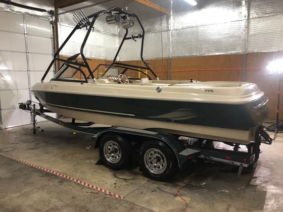 Cream and dark green ski boat with a black wake tower on a trailer inside the shop