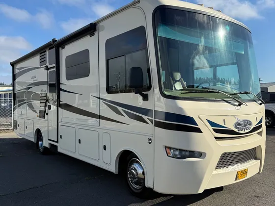 Cream Jayco Precept class A motorhome with blue and black graphics parked on a paved lot in daylight