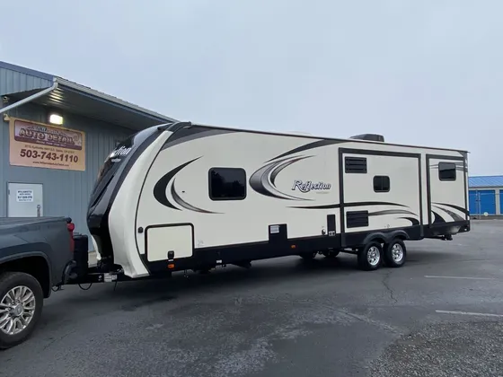Cream and black Reflection travel trailer hitched to a pickup in front of the shop on an overcast day