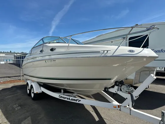 Cream cabin cruiser on a ShoreLand'r trailer parked in the lot, bow toward the camera