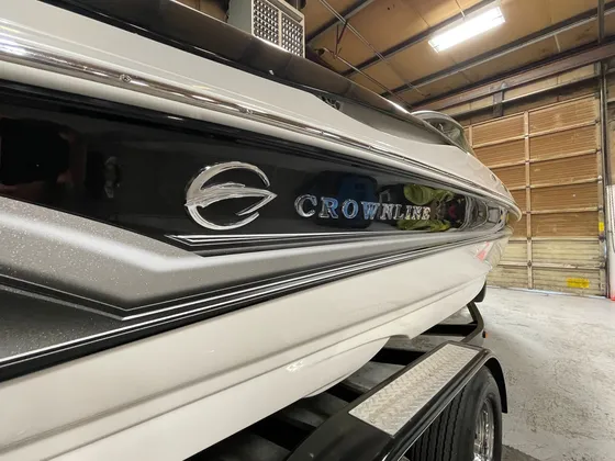 Close view of the Crownline badge and black stripe on the side of a white boat on its trailer in the shop