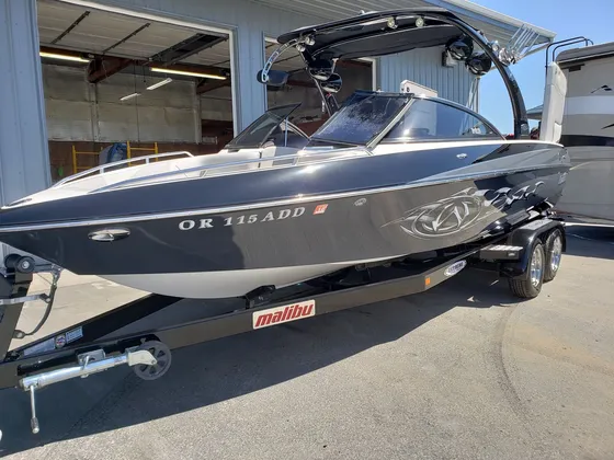 Dark gray and white Malibu wake boat on its trailer outside the shop