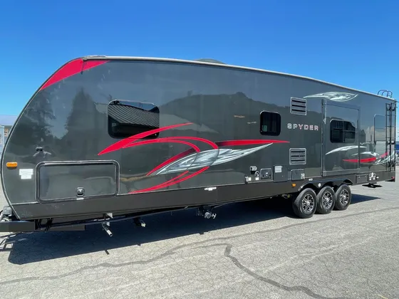 Dark gray Spyder travel trailer with red graphics and three axles parked on the lot in the sun
