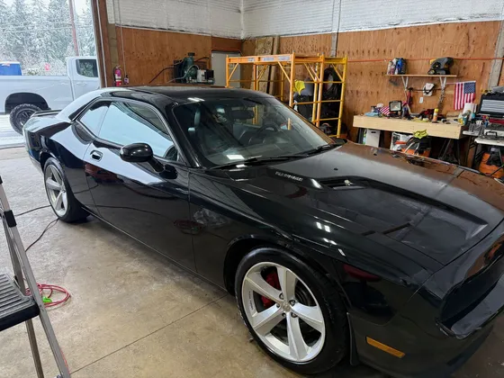 Black Dodge Challenger with silver wheels and red brake calipers parked inside the shop