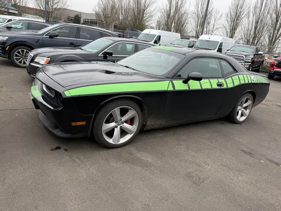 Black Dodge Challenger with green stripes and road spray on the lower doors, parked in a lot