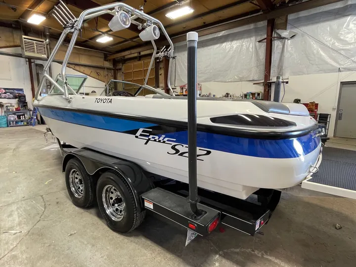 White and blue Epic S22 boat with a wake tower on a tandem-axle trailer inside the shop