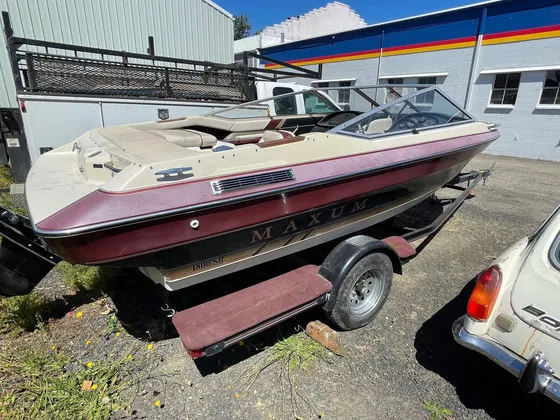 Maroon and tan Maxum 1800 SR runabout with a chalky dull deck sitting on a trailer in a gravel lot