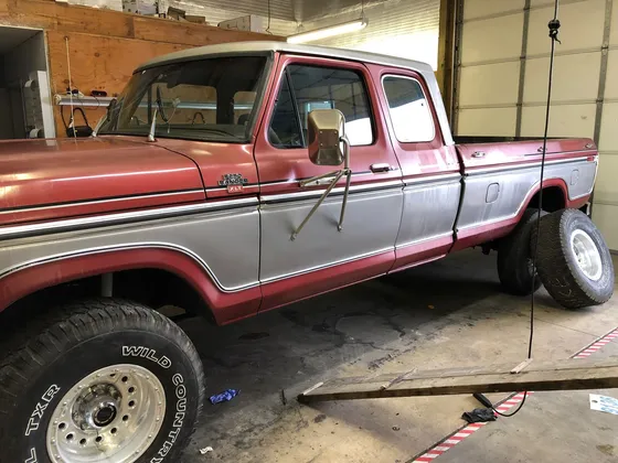 Older red and silver Ford F-250 Ranger XLT crew cab with faded paint inside the shop