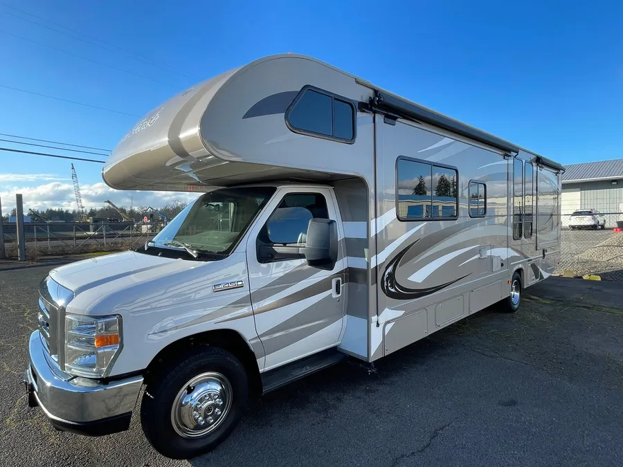 Tan and white Four Winds Class C motorhome on a Ford E-450 chassis parked outside under a blue sky