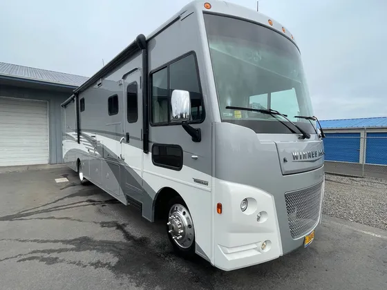 Gray and white Winnebago Class A motorhome parked on wet pavement, front passenger side