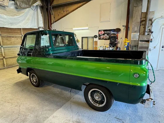 Two-tone green 1960s cab-forward pickup with chrome bumper and steel wheels in the shop