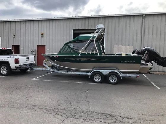 Green and tan Intruder aluminum boat with a hardtop on a trailer behind the shop truck, side view