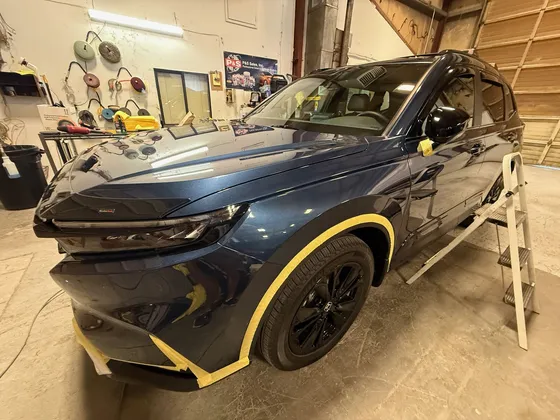 Dark blue Honda CR-V in the shop with yellow masking tape around the wheel arch and bumper