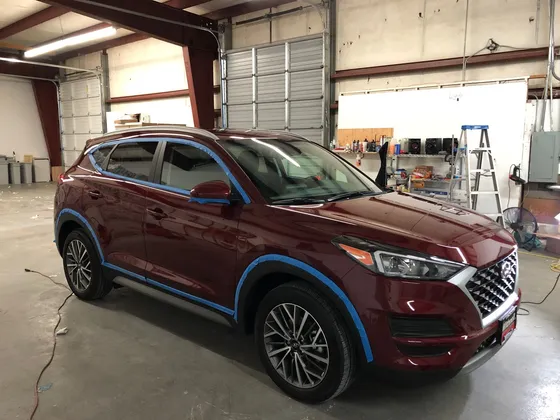 Dark red Hyundai SUV with blue tape along the fender edges and door trim inside the shop